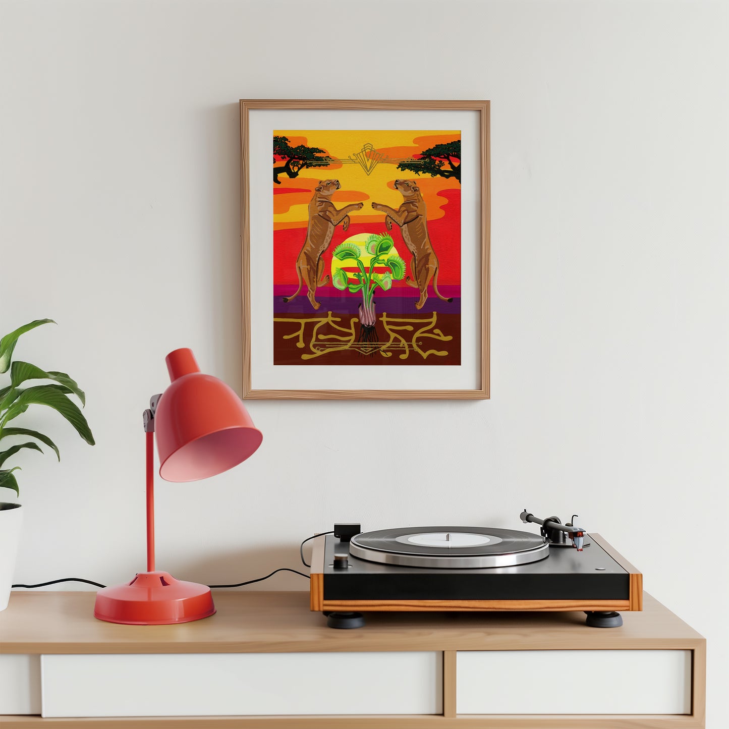 A framed art print featuring two lionesses leaping towards a bright sun is displayed on a white wall above a wooden console table with a red lamp and a turntable.