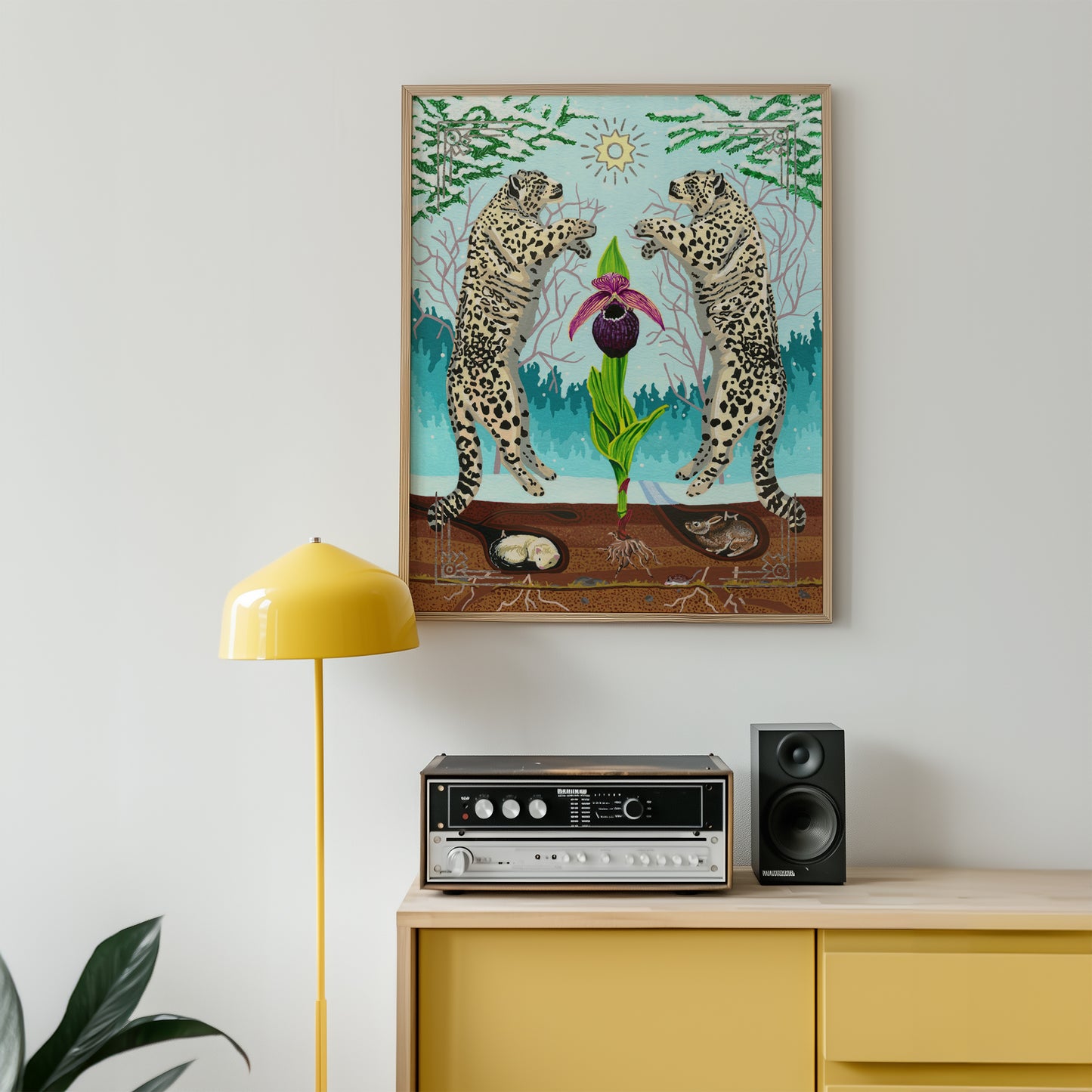 A framed art print depicting two snow leopards facing a purple and pink orchid flower hangs on a white wall above a yellow cabinet with a yellow floor lamp and a stereo system.
