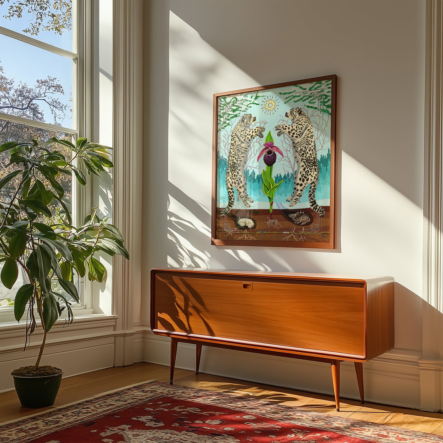 A framed art print depicting two snow leopards facing a central flower hangs on a light-colored wall above a mid-century modern wooden sideboard, with a potted plant and a red patterned rug in a sunlit room.