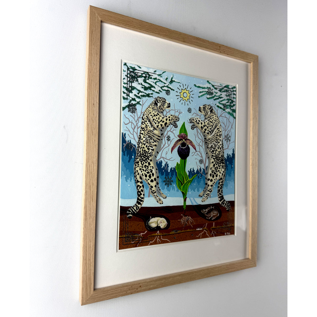 Angled side-view of the light oak wood framed snow leopard and orchid artwork mounted on a plain white wall, showcasing the frame's profile and depth.